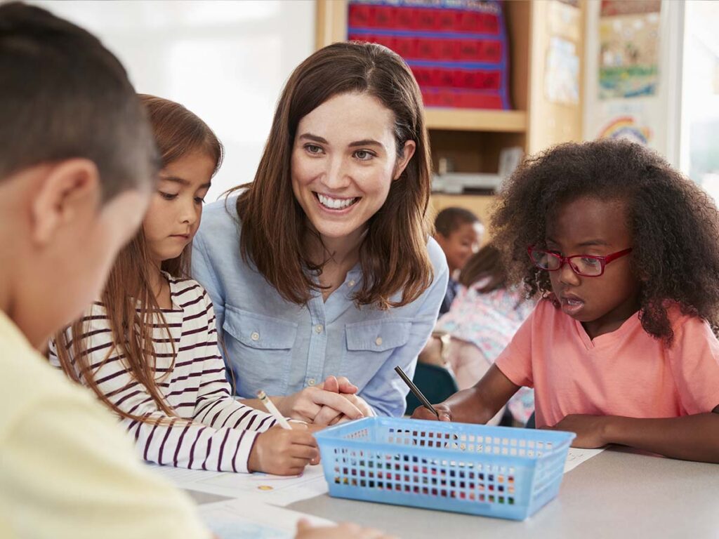 A teacher smiling while working at a table with her students